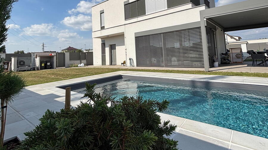 Okolo bazénu je dlažba a obrubní kámen v betonovém stylu